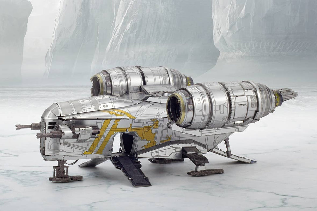 A silver and yellow Mandalorian Razor Crest Star Wars Premium Metal Earth DIY spaceship by Metal Earth is parked on an icy surface, with rocky cliffs and frosty terrain in the background.