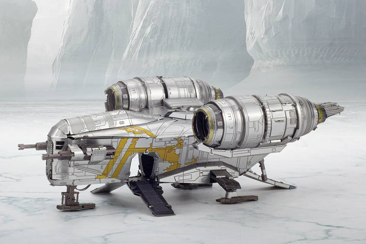 A silver and yellow Mandalorian Razor Crest Star Wars Premium Metal Earth DIY spaceship by Metal Earth is parked on an icy surface, with rocky cliffs and frosty terrain in the background.