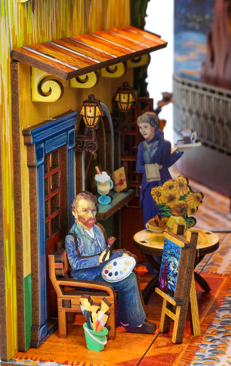 Hands Craft’s DIY Book Nook Kit: Vincent's World is a vibrant 3D paper diorama depicting an artist painting sunflowers at a café table as a woman serves tea—a charming Van Gogh-inspired bookshelf insert or architectural miniature.