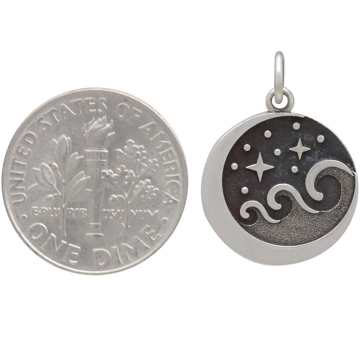 A U.S. dime beside the Nina Designs Starry Night Wave Pendant—a round sterling silver charm with crescent moon, stars, and wavy lines evoking oxidized night skies—shows the celestial pendant's size.