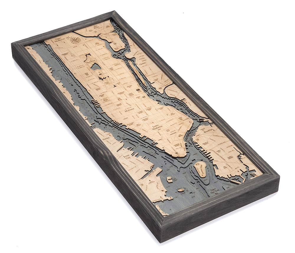 The WoodChart Manhattan 13.5" x 31" Grey Frame is a rectangular wooden map with topographic etching of NYC's Manhattan, featuring dark gray water areas and light wood streets, parks, and blocks, all presented at an angle.