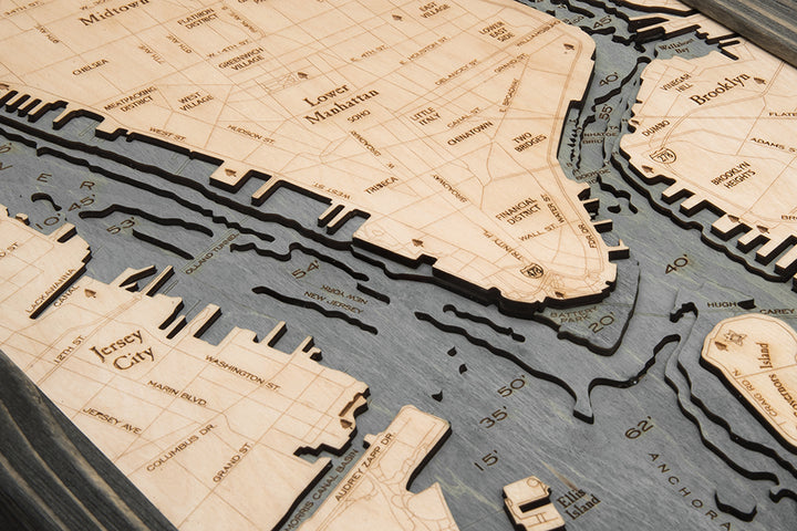 The WoodChart Manhattan 13.5" x 31" Grey Frame is a detailed wooden map with engraved labels for streets, neighborhoods, and landmarks in Lower Manhattan, Jersey City, Brooklyn, and the Hudson River.