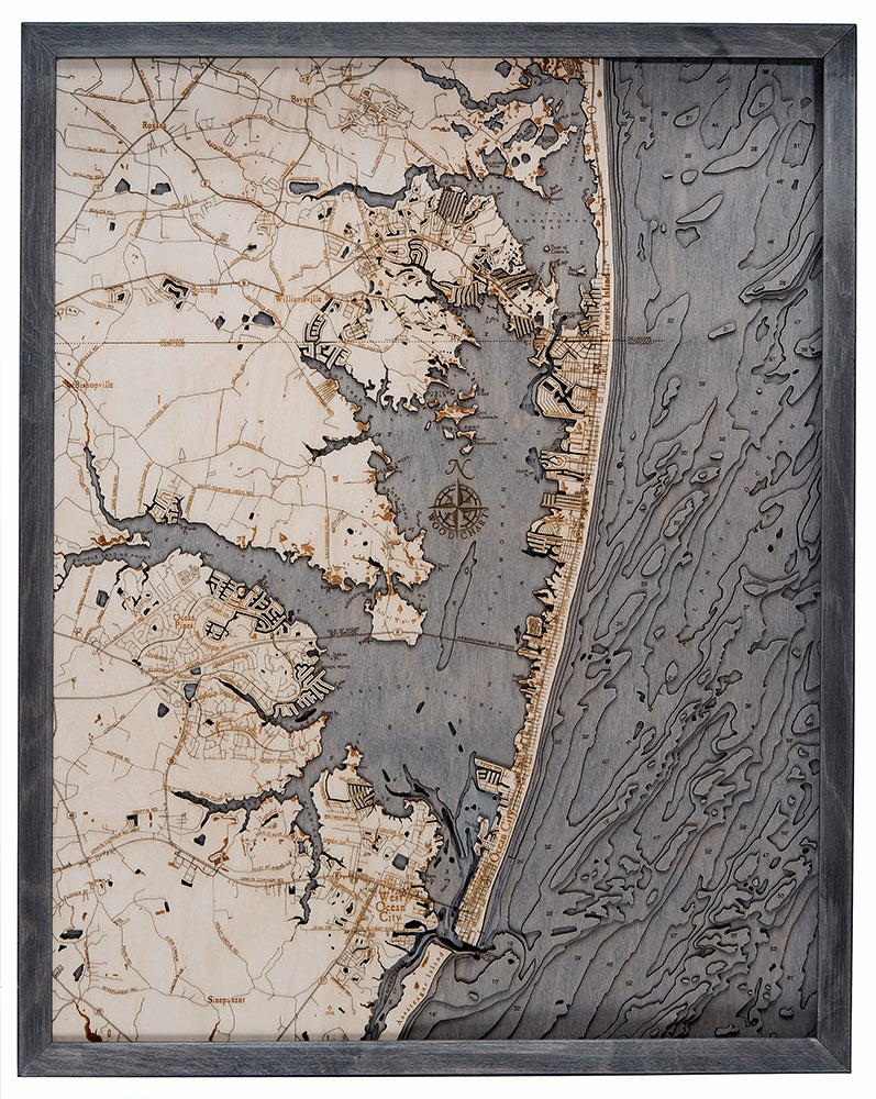 The WoodChart Ocean City MD 24.5 x 31 Grey Frame map displays detailed towns, roads, shoreline, and waterways with textured ocean patterns on the right and finely crafted city streets and buildings on land.