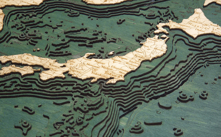 WoodChart’s Japan Korea 16" x 20" Black Frame features a detailed wooden topographic map of Japan and nearby regions, with layered contours and labeled cities like Tokyo and Yokohama on a green background.