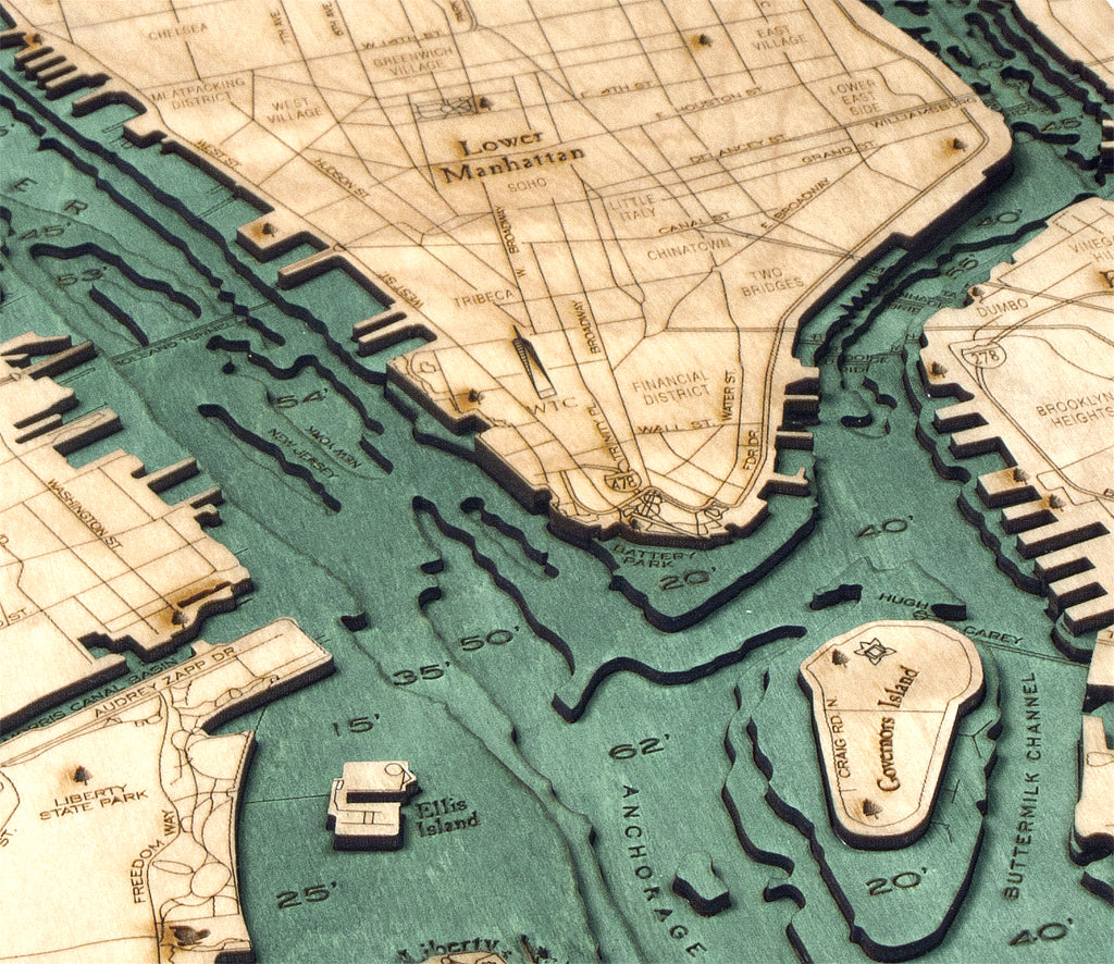 A close-up of WoodChart's Manhattan 13.5" x 31" Black Frame: a wooden carved map with engraved labels and depth markings, depicting Lower Manhattan, nearby waterways, Ellis Island, the Statue of Liberty, and Governors Island.