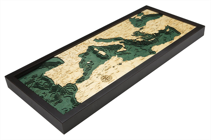 The WoodChart Mediterranean Sea 13.5" x 31" Black Frame map features a topographic, layered wood design with green water, highlighting Europe, North Africa, and the Middle East.