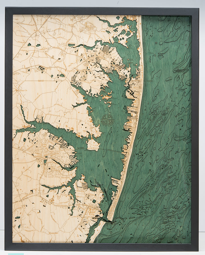 The WoodChart Ocean City MD 24.5 x 31 Black Frame features a detailed wooden map with etched city buildings by the shore, beige land on the left, and green-tinted water on the right—all in a sleek black frame.