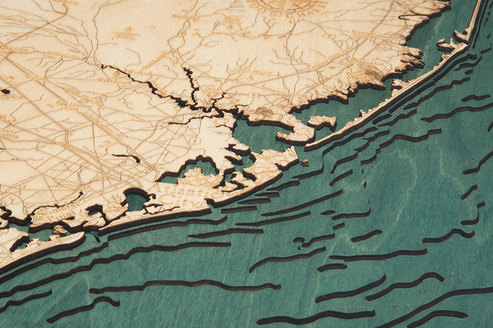A close-up of the WoodChart Ocean City MD 24.5 x 31 Black Frame map showcases detailed laser-etched coastlines and ocean, with engraved contours and blue tones depicting the sea.