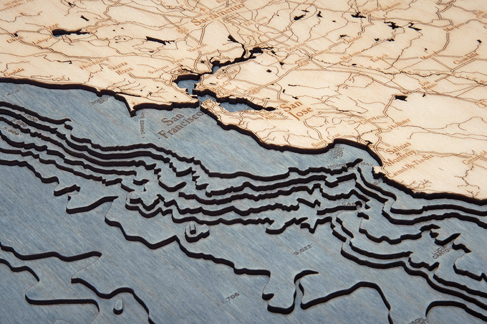 The WoodChart California Coast 24.5" x 31" White Frame is a wooden relief map featuring engraved cities, roads, and layered topography, showcasing both land and water features along the California coast.