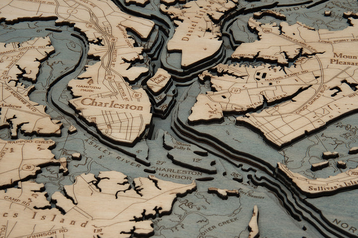 The WoodChart CharlstonSC 24.5 x 31 White Frame is a layered wooden map featuring Charleston, SC and surroundings, with engraved place names, roads, and blue water accents on natural wood.