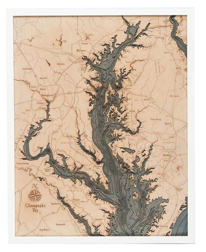 The WoodChart Chesapeake Bay 24.5" x 31" map, set in a white frame, displays detailed water depths, labeled towns and cities, engraved accents, and a decorative compass rose of the Chesapeake Bay and its surroundings.