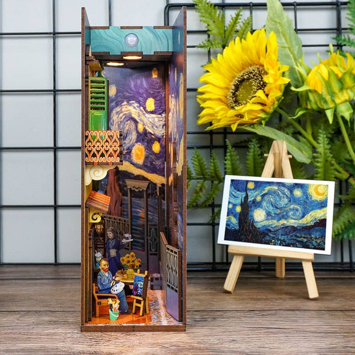 The Hands Craft DIY Book Nook Kit: Vincent's World is a miniature diorama inspired by Van Gogh’s "Starry Night," featuring café figures, a sunflower, green ferns, and a small easel with the iconic artwork for a charming bookshelf display.