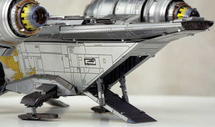 Close-up of the Mandalorian Razor Crest Star Wars Premium Metal Earth DIY by Metal Earth, featuring metallic textures, two large engines, and an extended boarding ramp. The soft-focus background highlights this impressive collector’s kit.