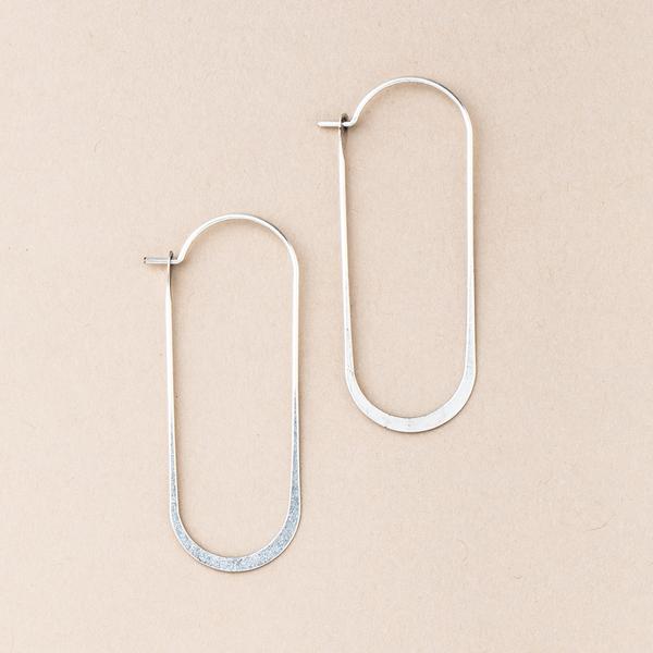 The Cosmic Oval Silver earrings by Scout Jewelry, featuring minimalist and elongated silver hoops with a flat base, are showcased against a light beige background. These rectangular-shaped earrings, made from hypoallergenic 925 sterling silver, have rounded edges and boast a smooth, polished finish.