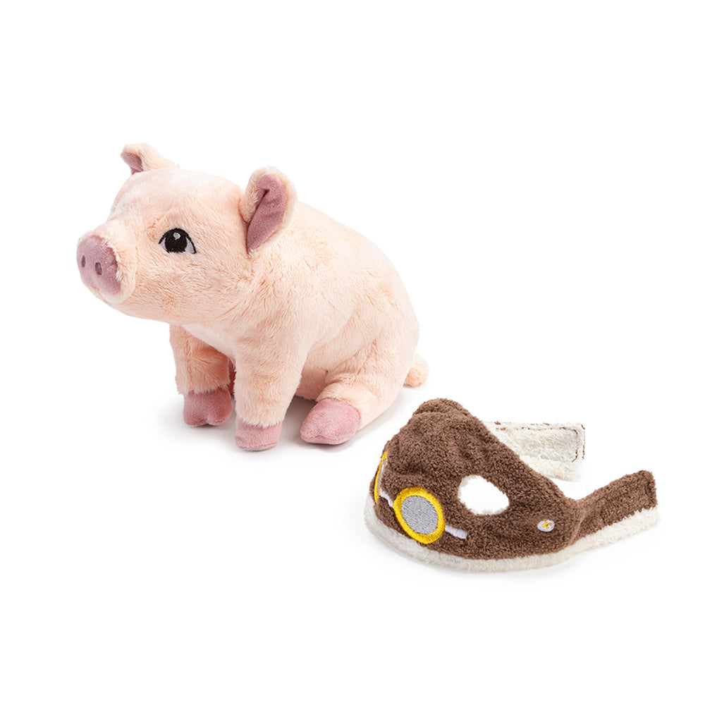A Compendium Flying Pig Plush with soft, pink fur and an adorable face is sitting on its back legs. Next to it rests a separate brown, stuffed half-mask featuring yellow circular details that resemble aviator goggles—an ideal gift for dreamers.