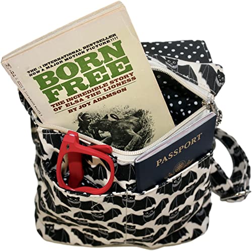 The Sm Messenger Bat by Bungalow 360, crafted from natural durable cotton canvas with a polka dot interior fabric and a secure zipper closure, showcases unique black-and-white cat designs. This stylish bag holds a partially visible copy of "Born Free" by Joy Adamson, along with a passport and red-framed eyeglasses.