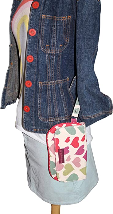 A mannequin is dressed in a denim jacket with red buttons, a white shirt featuring a colorful heart design, and a light blue skirt. It carries the "Large Wristlet Hearts" by Bungalow 360, adorned with multicolored hearts and a branded patch, showcasing unique designs.