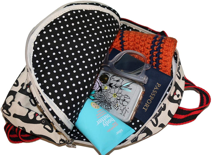 A Backpack Bat by Bungalow 360, featuring a black and white patterned cotton canvas exterior with red handles, contains a blue body butter tube, a smartphone adorned with a floral case, a pair of clear glasses, an orange knit hat, and a passport. The interior showcases unique designs with black fabric and white polka dots.