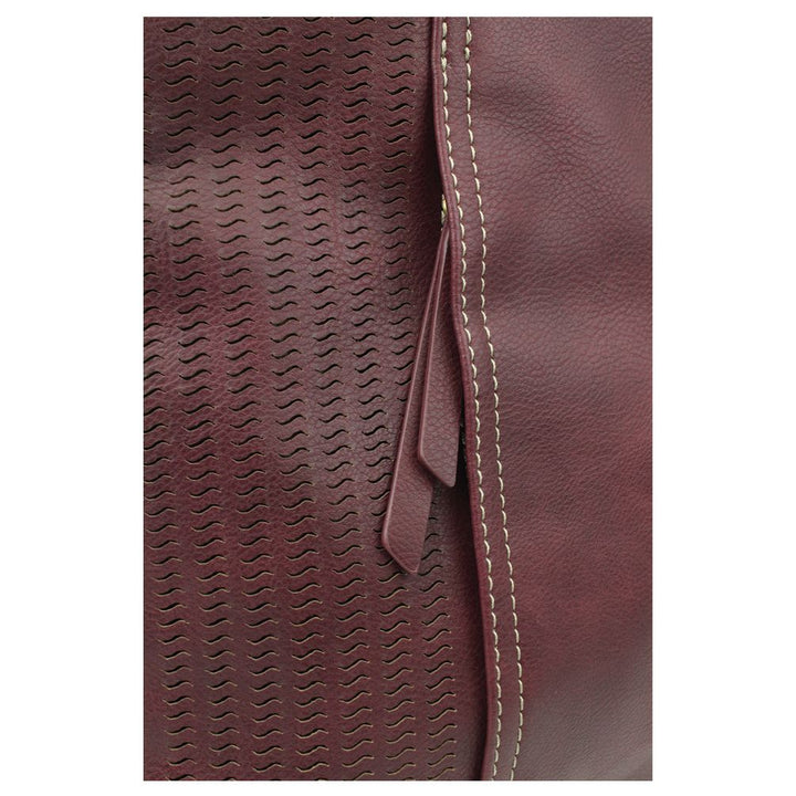 Close-up of textured faux plum leather from the Lasercut Crossbody DF by Chala, featuring a wavy laser-cut pattern on the left and a smooth surface on the right. A vertical seam with contrasting white stitching runs along the edge, adorned with a leather loop detail.