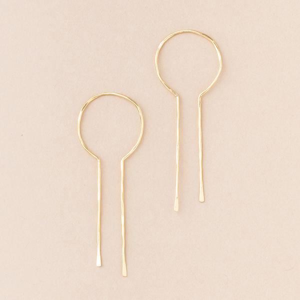 Presenting the Equinox Keyhole Hoop Gold earrings by Scout Jewelry: a pair of minimalist 18K Gold Vermeil earrings with circular shapes at the top and elongated, thin drops extending downwards. Set against a plain beige background, their design is simple and elegant, showcasing a modern, delicate aesthetic while being hypoallergenic and nickel- and cadmium-free.
