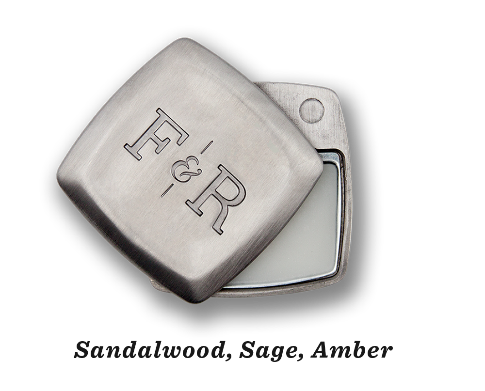 A metal container engraved with "Fulton & Roark" on the lid, slightly open to reveal Blue Ridge .2oz, a solid substance exuding the rich scents of sandalwood, sage, and amber.
