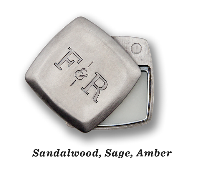 A metal container engraved with "Fulton & Roark" on the lid, slightly open to reveal Blue Ridge .2oz, a solid substance exuding the rich scents of sandalwood, sage, and amber.