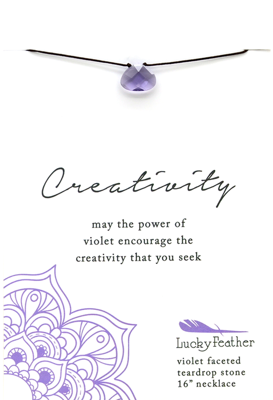 The Power Necklace Violet Creativity by LuckyFeather is showcased above, featuring a teardrop-shaped violet stone with a faceted gem on a sleek black cord. The accompanying text states: "Creativity: may the power of violet, your ultimate power color, inspire the creativity you seek." To complete the presentation, an elegant lavender pattern decorates the bottom.