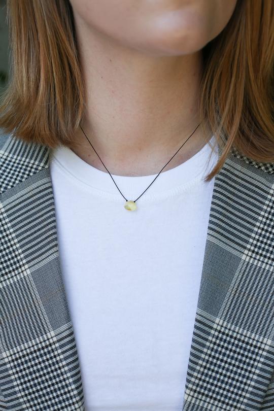 A person is adorned with a white t-shirt underneath a plaid blazer, complemented by the Power Necklace Yellow Strength from LuckyFeather. The image draws attention to the neck and shoulders without any visible facial features, showcasing the understated elegance and powerful hue of this accessory.