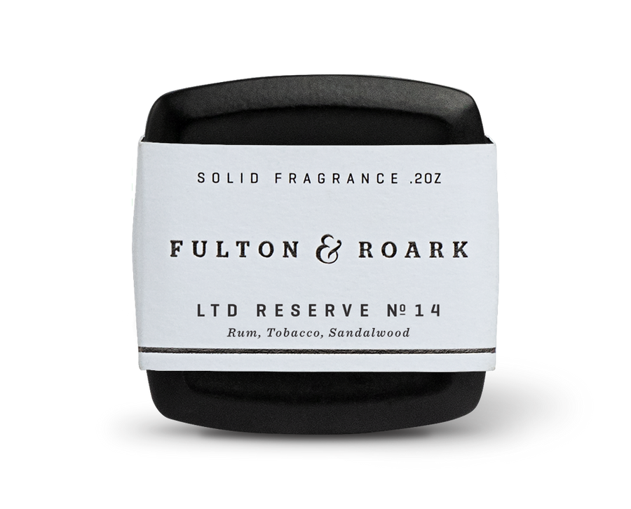 A small, sleek black container of solid fragrance from Fulton & Roark. The label reads "Calle Ocho .2oz," and the scent details below conjure up notes of Rum Tobacco, Sandalwood. The container lies on a white surface, casting a slight shadow reminiscent of Calle Ocho's vibrant charm.