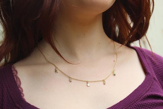 Close-up of a person wearing the elegant Dangle Necklace Shine by LuckyFeather, featuring small crescent moon and star charms in a 14k gold plated design. This adjustable necklace beautifully complements the purple top, while long, brown hair cascades gracefully over the shoulders.