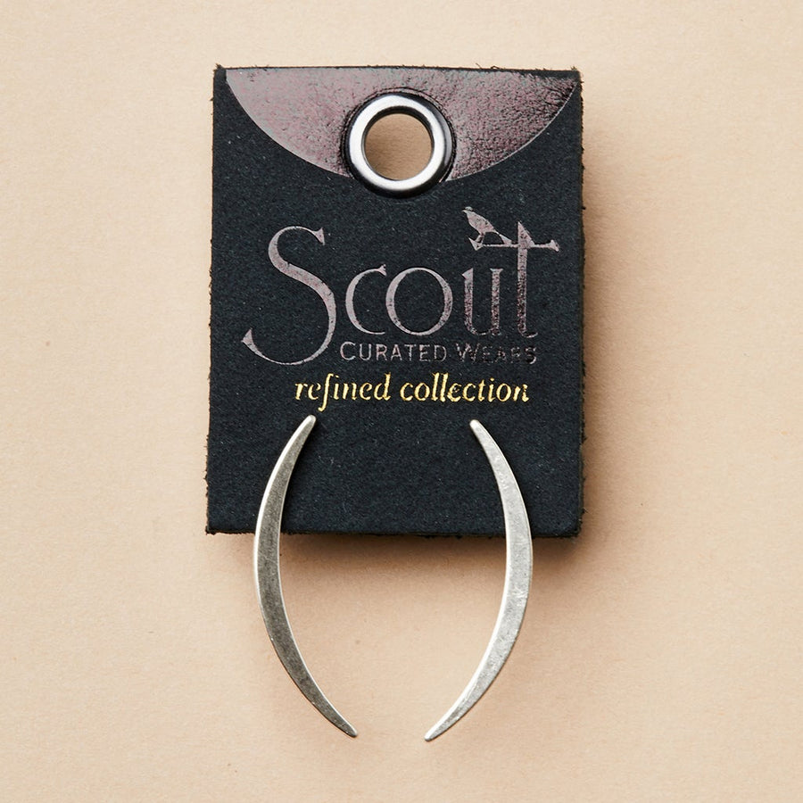 A pair of Gibbous Slice Stud Silver earrings from Scout Jewelry, made of 925 sterling silver, is displayed on a black card labeled "Scout Curated Wears - Refined Earring Collection," featuring a bird illustration and a circular hole against a light beige background.