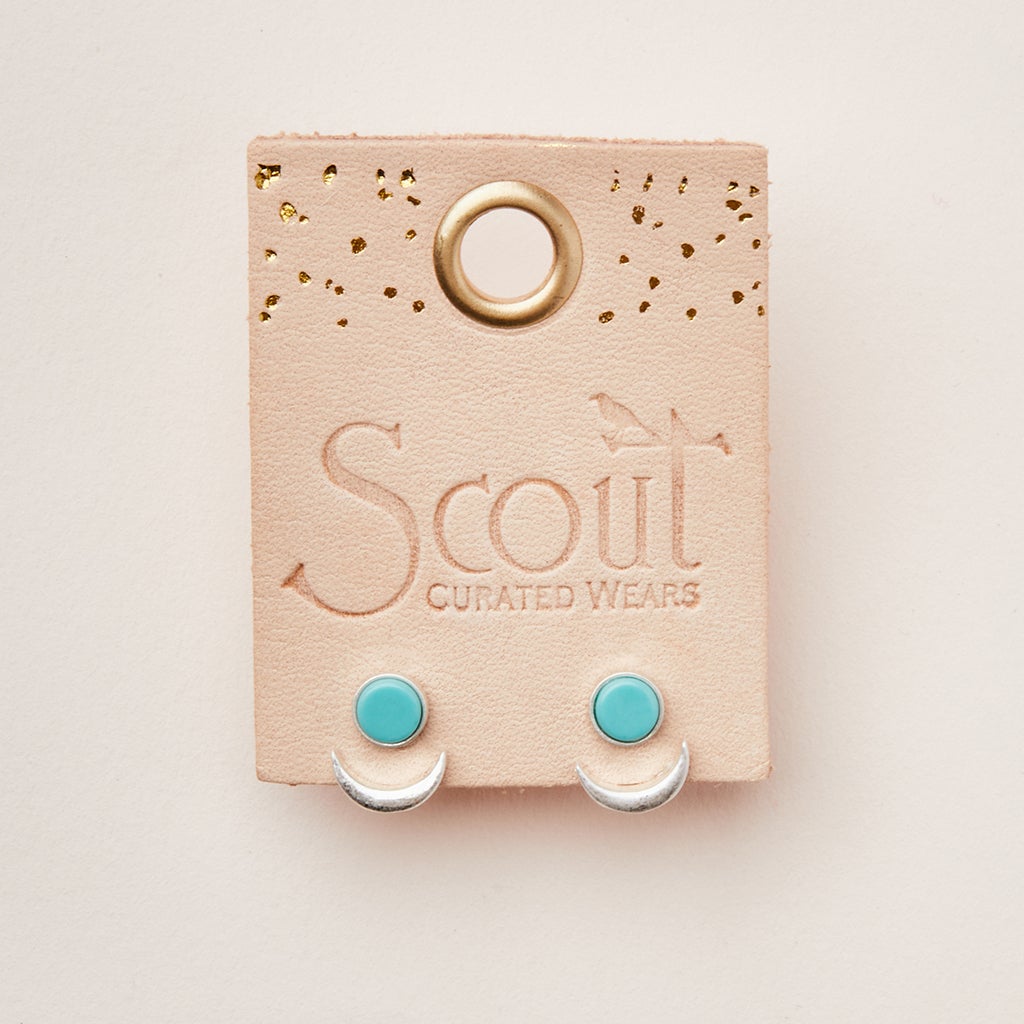 A pair of Moon Phase Turquoise/Silver earrings from Scout Jewelry is displayed on a beige card with "Scout Jewelry" elegantly embossed on it. The card features a gold hole at the top and decorative gold dots, enhancing the beauty of the hypoallergenic earrings.