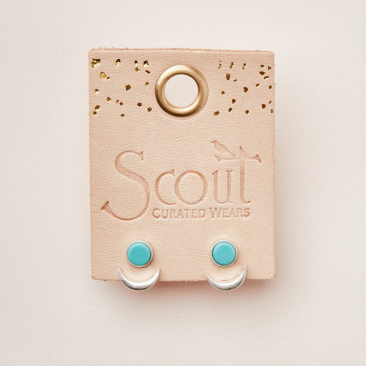 A pair of Moon Phase Turquoise/Silver earrings from Scout Jewelry is displayed on a beige card with "Scout Jewelry" elegantly embossed on it. The card features a gold hole at the top and decorative gold dots, enhancing the beauty of the hypoallergenic earrings.