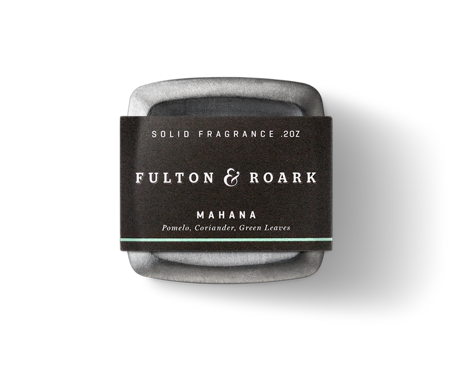 Fulton & Roark's Mahana solid fragrance, weighing 0.2 ounces, is housed in a square metal container with a black label. The fragrance captures the essence of Green Sand Beach with notes of pomelo, coriander, and green leaves, reminiscent of Papakolea's lush surroundings.