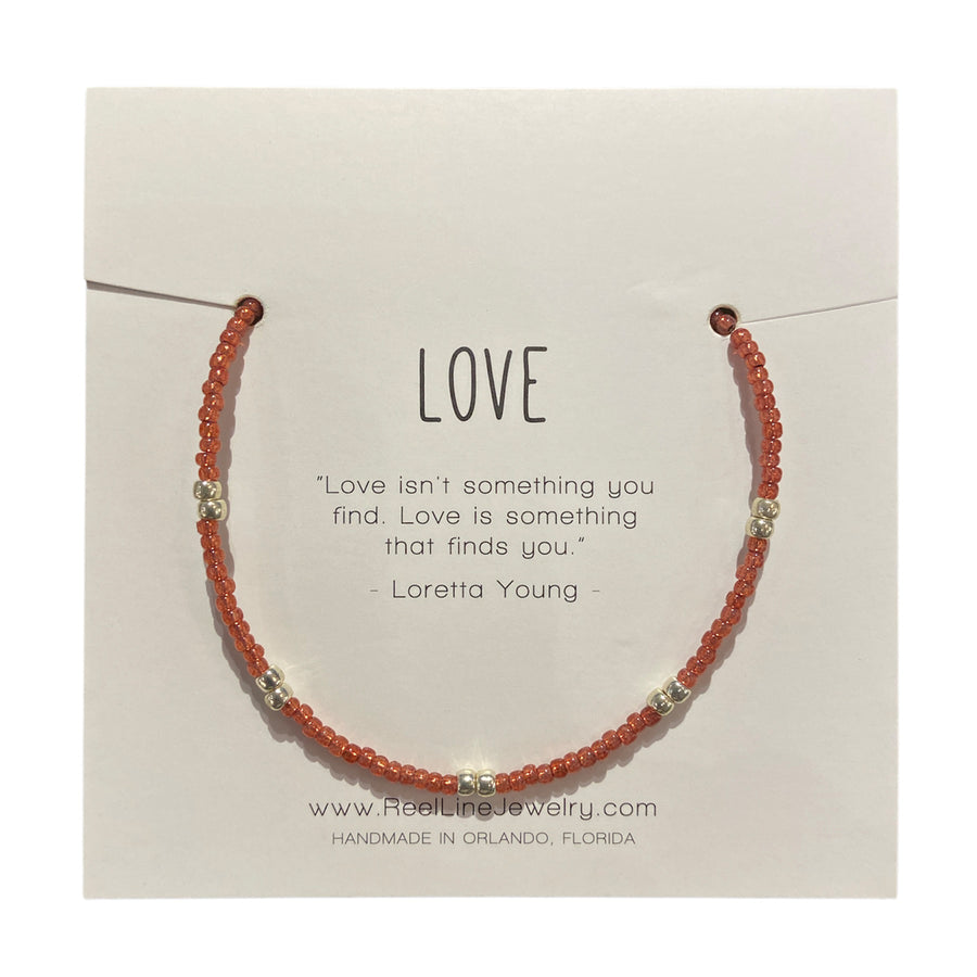 The "Love - Pomegranate and Silver" bracelet by Reel Line Jewelry is a thin, beaded piece on a card with an inspirational quote on love by Loretta Young, handcrafted in Orlando with adjustable links.