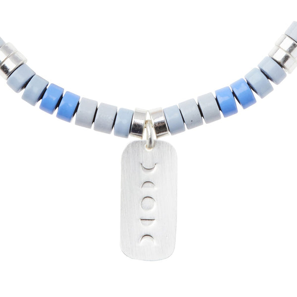 The Intention Charm Howlite Silver necklace by Scout Jewelry showcases a range of semi-precious stones in hues of blue and gray, highlighted by a central sterling silver dipped charm pendant engraved with four crescent moon phases.