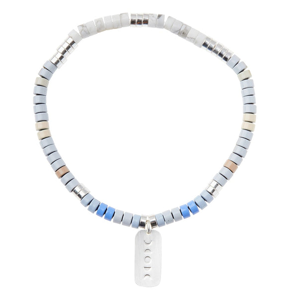 The "Intention Charm Howlite Silver" bracelet by Scout Jewelry features a stylish blend of blue, gray, and beige semi-precious stones along with a small rectangular silver tag embossed with symbols to inspire positive intentions.
