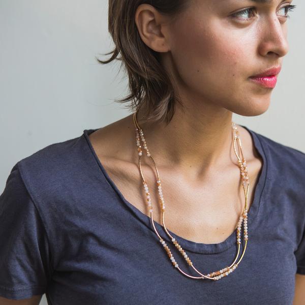 A person is wearing a dark gray t-shirt complemented by Scout Jewelry's "She Believed She Could" layered necklace in ivory combo and gold, looking to the side against a plain light-colored background.