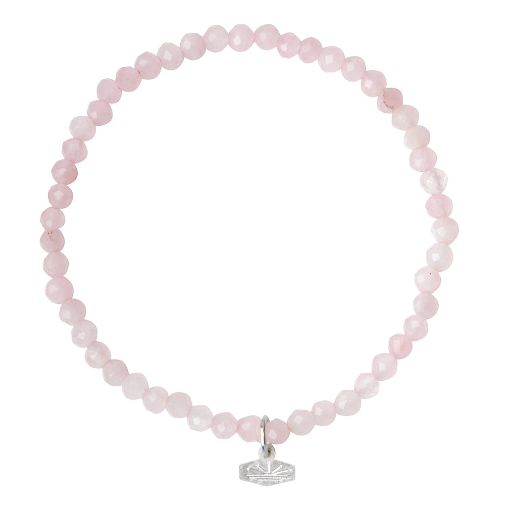 Experience the elegance of the Mini Bracelet Rose Quartz/Silver by Scout Jewelry. This delicate bracelet features small, round rose quartz beads strung together on a stretch cord, creating an elegant design. A small silver charm with an etched leaf pattern dangles gracefully from the bracelet, adding a subtle decorative touch. The semi-precious gemstones are set against an all-white background for a timeless look.