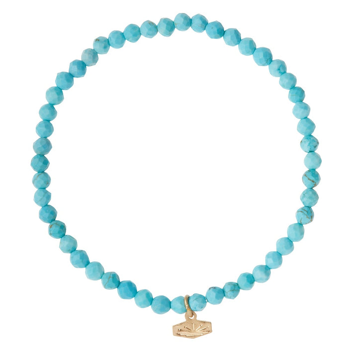 Introducing the Mini Bracelet Turquoise/Gold by Scout Jewelry—a charming accessory featuring small, round, faceted turquoise semi-precious gemstones. This bracelet is accented with a delicate gold-tone charm engraved with a star-like design. Strung on a convenient stretch cord, its circular arrangement elegantly highlights both its form and intricate details.