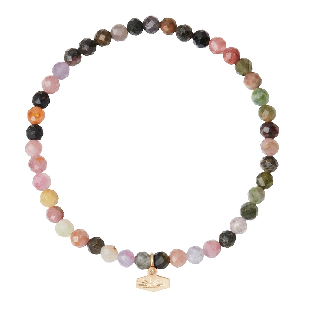 Introducing the Mini Bracelet Tourmaline/Gold by Scout Jewelry: a vibrant multicolored bracelet featuring semi-precious tourmaline gemstones in captivating shades of pink, green, brown, and purple. The faceted stone beads are elegantly strung on a stretch cord, adorned with a small gold charm that displays the brand's logo.