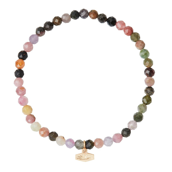 Introducing the Mini Bracelet Tourmaline/Gold by Scout Jewelry: a vibrant multicolored bracelet featuring semi-precious tourmaline gemstones in captivating shades of pink, green, brown, and purple. The faceted stone beads are elegantly strung on a stretch cord, adorned with a small gold charm that displays the brand's logo.