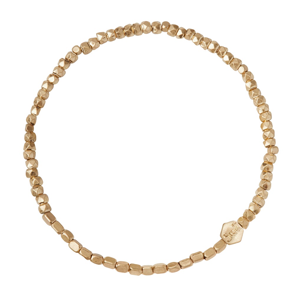 The Mini Metal Bracelet Gold by Scout Jewelry is a delicate piece featuring small, irregularly shaped gold and brass beads strung together. One hexagonal bead with an engraving adds a unique touch to the minimalist design. This bracelet forms a complete circle on a stretch cord for easy wear.