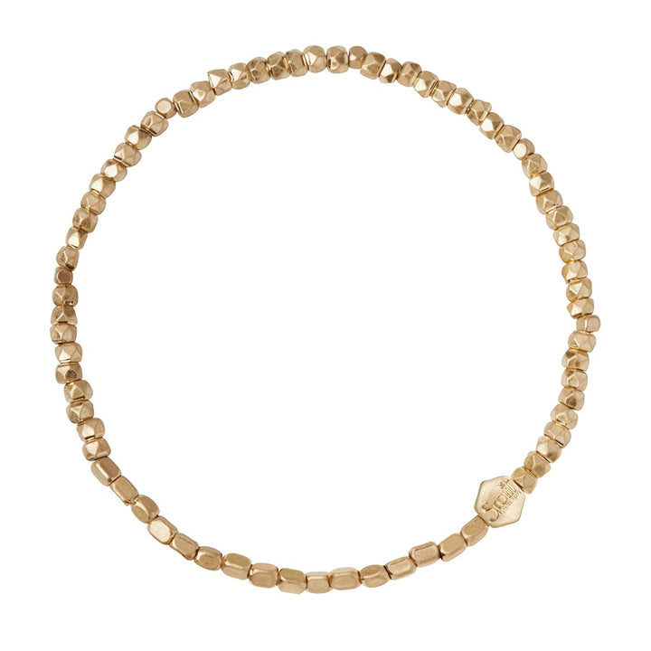 The Mini Metal Bracelet Gold by Scout Jewelry is a delicate piece featuring small, irregularly shaped gold and brass beads strung together. One hexagonal bead with an engraving adds a unique touch to the minimalist design. This bracelet forms a complete circle on a stretch cord for easy wear.