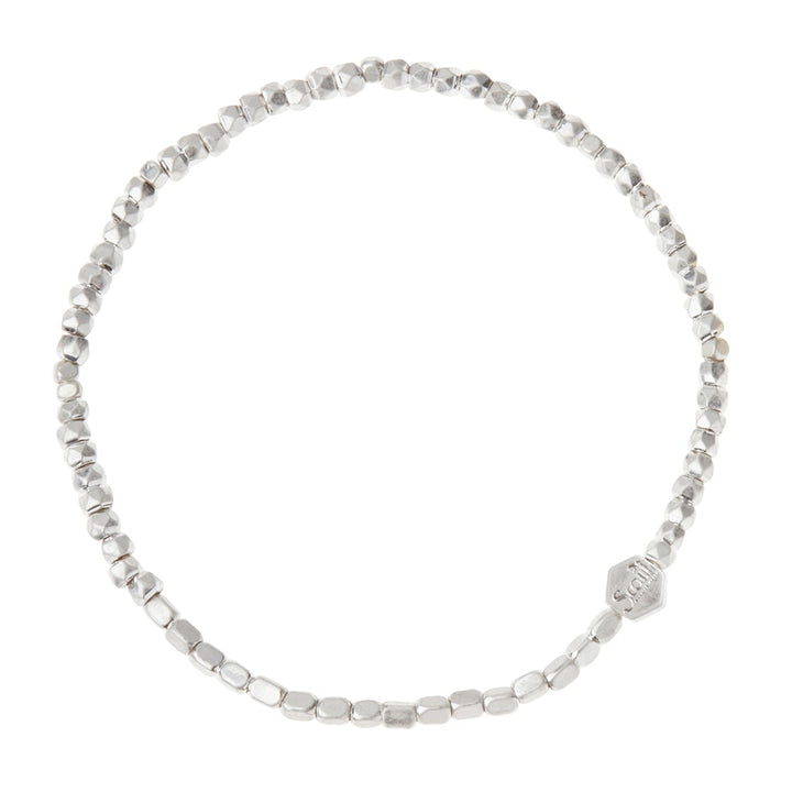 A close-up image of the Scout Jewelry Mini Metal Bracelet Silver, featuring small, irregularly shaped silver beads strung on a stretch cord. The circular bracelet includes a small hexagonal charm with text on it and showcases mixed metals for subtle accents against a plain white background.