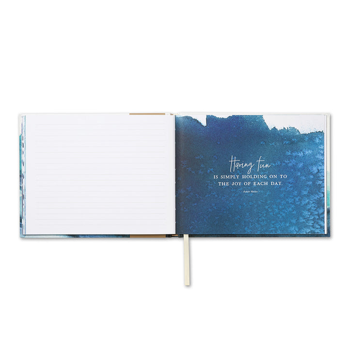The Swept Away Coastal Guest Book by Compendium captures meaningful moments with its unique layout: a blank lined page on the left and a blue abstract page on the right, adorned with the quote "Having fun is simply holding on to the joy of each day." It comes with a white ribbon bookmark.