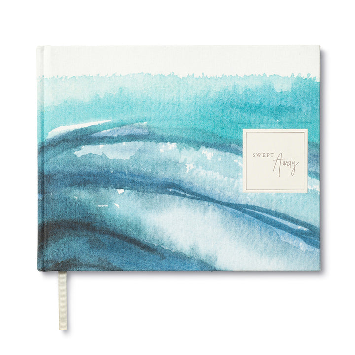 Introducing the Swept Away Coastal Guest Book by Compendium—a journal designed to capture everyday joys with its watercolor wave design in shades of blue and turquoise. The cover boasts a square label featuring "Swept Away" in elegant script. Ideal for use as a guest book, it includes a cream-colored ribbon bookmark to highlight meaningful moments.