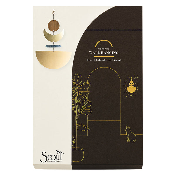 Packaging for the Moonrise Labradorite Wall Hanging, incorporating sculptural elements made of brass and wood. The design presents a minimalist illustration featuring a plant, a cat, and decorative arches on a black and beige background. The brand name "Scout Jewelry" is prominently displayed.