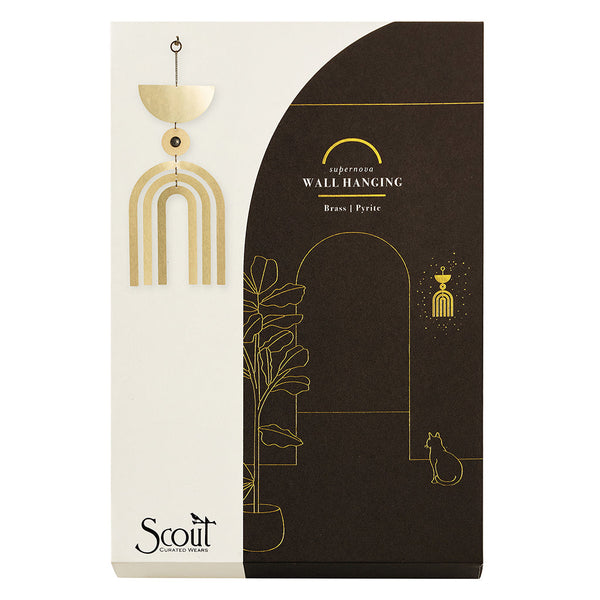 The packaging of the Supernova Pyrite Wall Hanging by Scout Jewelry showcases a minimalistic design with a brass and semi-precious stone motif. It includes a decorative arch and plant illustration, featuring a white and dark brown color scheme with an elegant cat figure on the right, reflecting the sophistication of sculptural wall art.