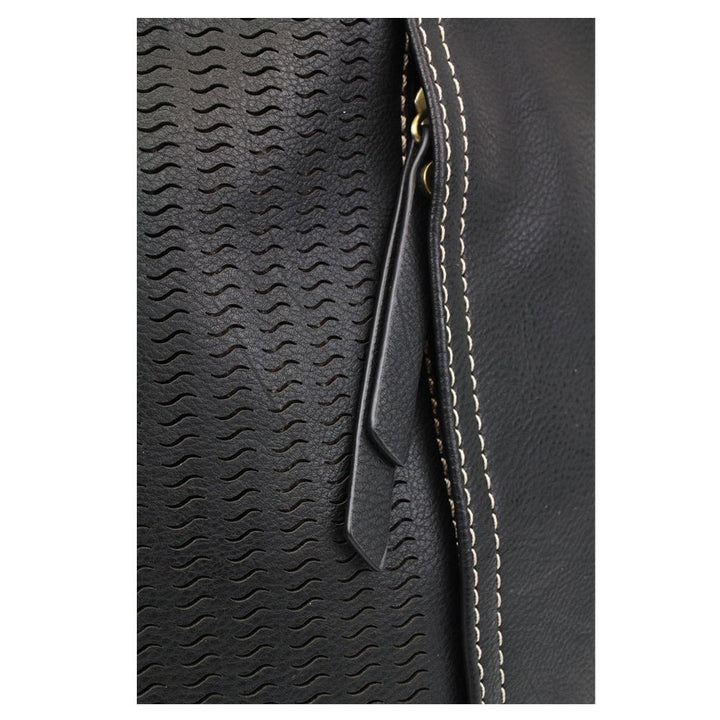 Close-up image of the Lasercut Crossbody DF Black by Chala, showcasing its textured wave patterns on the black faux leather surface and a partially visible gold zipper. White stitching lines along the edge adjacent to the zipper enhance its design. A prominent black leather zipper pull is centered for easy access.